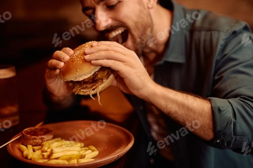 Preview: Close up of man eating burger in a bar.