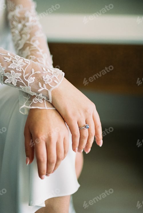 Preview: Bride in a white lace robe sits with her hands folded on her knees. Cropped. Faceless
