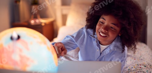Preview: Boy In Bedroom At Night Lying On Bed Using With Laptop With Illuminated Globe