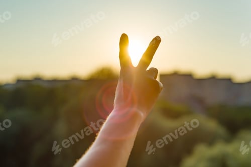 Preview: Hand showing two fingers or victory gesture. Background evening sunset, city silhouette