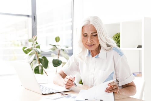Preview: Senior Woman Reviewing Documents at Desk with Laptop