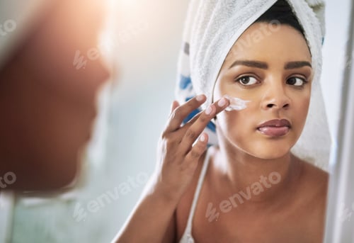 Preview: Shot of an attractive young woman applying moisturizer to her face in the bathroom
