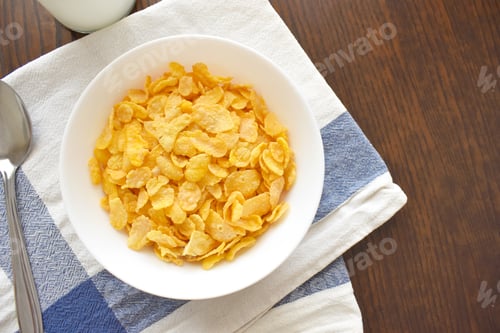 Preview: Cornflakes in a white bowl, a spoon and a bottle of milk on wood table.