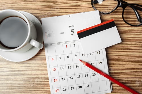 Preview: Busy workspace featuring calendar, coffee cup, and card on wooden table in May