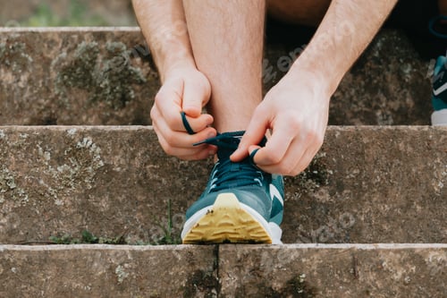 Preview: A super close up of a man tying the shoelaces on this sport shoes over concrete