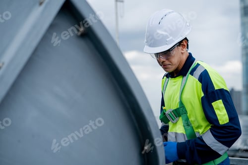 Preview: A man in a yellow and blue safety vest is working on a metal structure