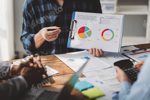 Preview: Young colleagues discuss business and analytical price charts using calculators and laptops to calcu