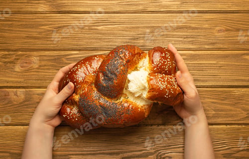 Preview: Female hands tearing off a piece of freshly baked Challah bread covered with poppy and sesame seeds