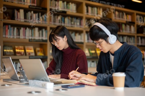 Preview: Glasses asian woman student and a man friend doing assignment together while sits at library's table