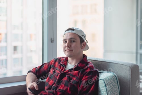 Preview: Casually dressed young man sitting by a window in high rise building