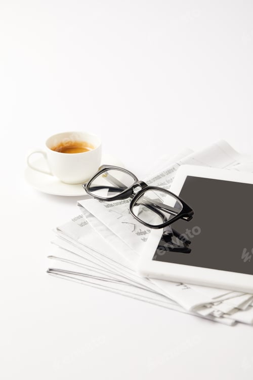 Preview: eyeglasses and digital tablet on pile of newspapers and coffee cup, on white