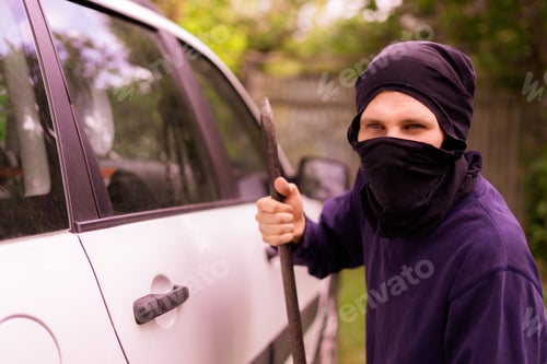 Preview: masked thief standing near the car and trying to smash the window with cowbar
