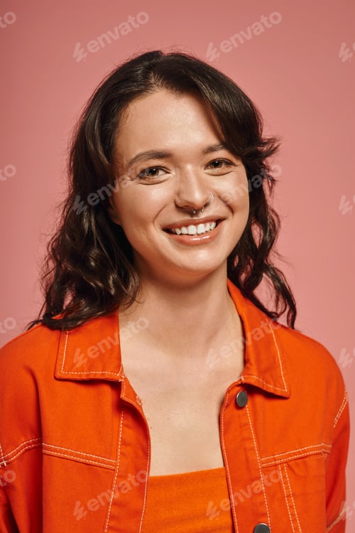 Preview: Young woman showcases modern fashion in vibrant orange attire against pink background