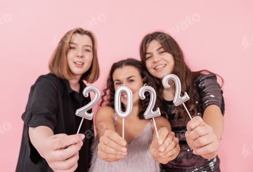 Visualização: Um grupo de garotas está segurando velas dos números 2022 em um fundo rosa.