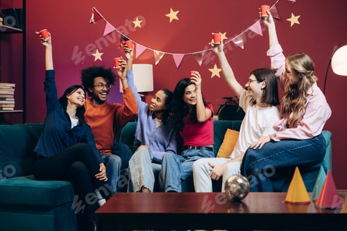Preview: Diverse group of multinational friends celebrating joyful party at home sitting on sofa