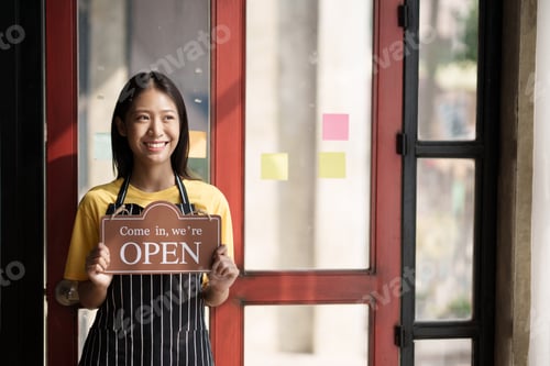 Preview: Small business owner smiling while turning the sign for the opening of the shop. Close up of woman