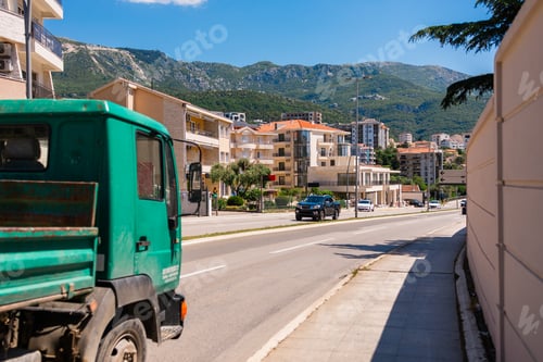 Preview: Urban street with moving vehicles and residential buildings against mountains.