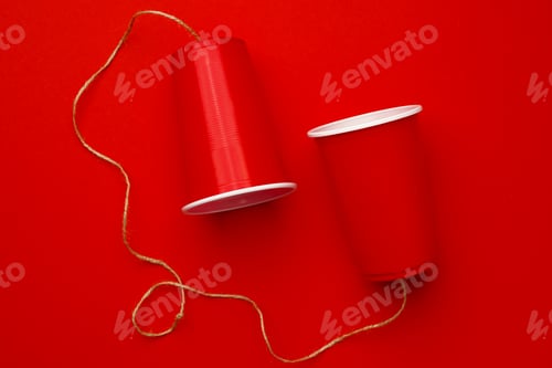 Preview: Red plastic cups connected with a thread on red background