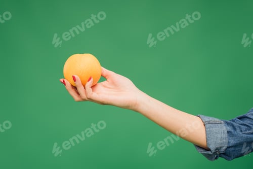 Preview: cropped view of woman holding orange in hand isolated on green