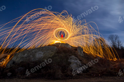 Preview: Long exposure shot of man standing on rocky hill spinning steel wool