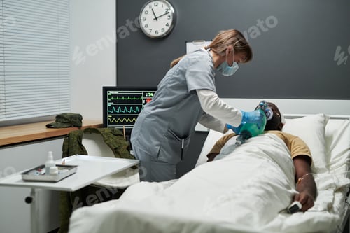 Preview: Nurse bending over patient while checking respiratory mask