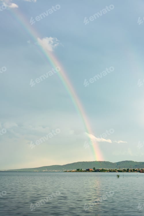 Preview: Multicolored beautiful rainbow over the river bay in the sky with clouds.