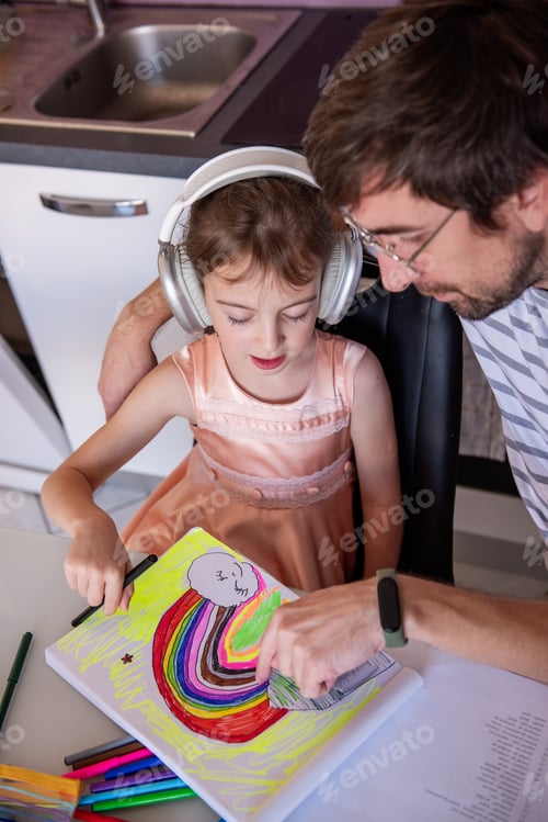 Preview: Father helping his daughter drawing a rainbow while wearing headphones