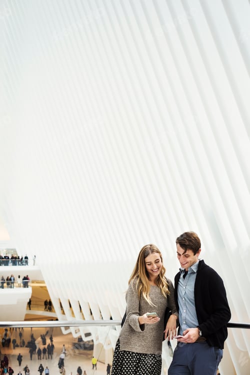 Preview: Two people standing on a balcony sharing a phone screen, with an overview of the central atrium of