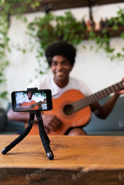 Preview: African american man recording guitar online lesson with phone. Selective focus on phone. Vertical.