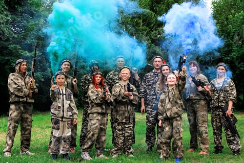 Preview: People in camouflage celebrating winning laser tag shooting game with colored smoke. N