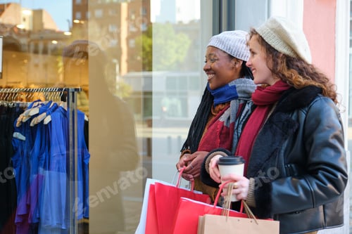 Preview: Two multiracial female friends looking at shop window in the city.