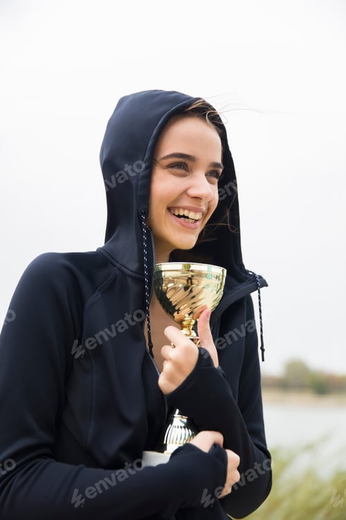 Preview: Happy sporty young woman holding gold trophy cup