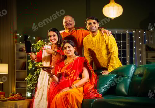 Preview: Holding smartphone during Diwali fest, happy Indian family promotes app at decorated cozy home