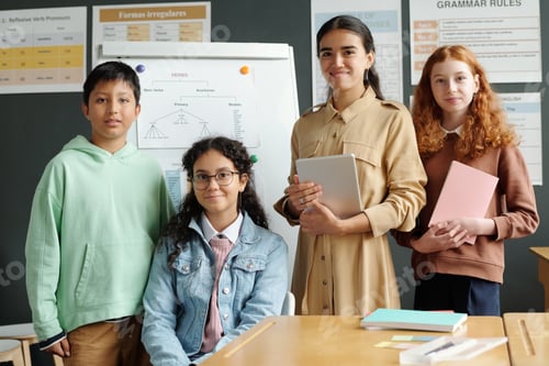Preview: Happy young English teacher with tablet and group of intercultural learners