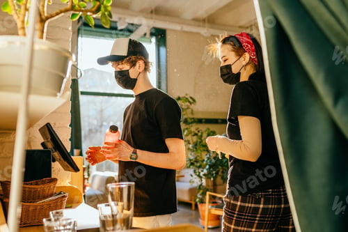 Preview: Handsome cashier in protective mask using digital device for payment.
