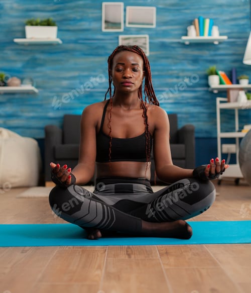 Preview: Calm tranquil black woman keeping eyes closed sitting on yoga mat
