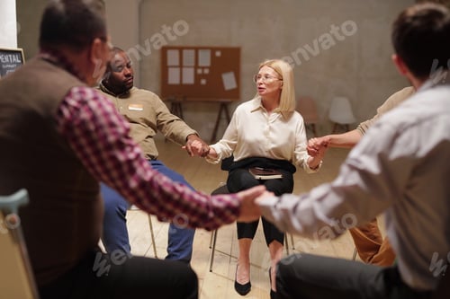 Preview: Several patients of mental support group holding by hands during session while sitting in circle