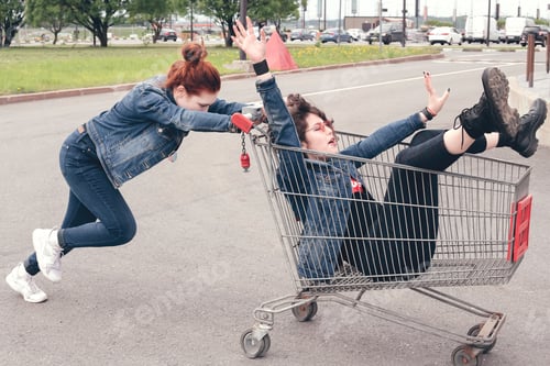Preview: ✓ ↟ Funny happy teenage girls in denim clothes have fun and ride on the shopping cart