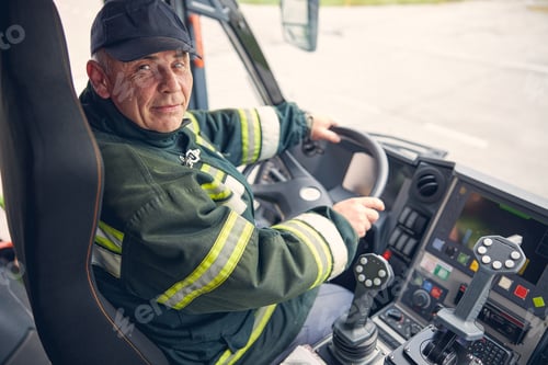 Preview: Portrait of happy mature firefighter driving firetruck