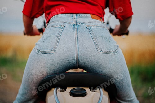 Preview: Buttocks of a young woman in stylish jeans on the seat of a motor scooter. back view. sexy ass.