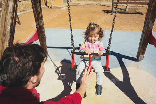 Preview: Toddler girl playing with dad sitting in a swing at the playground