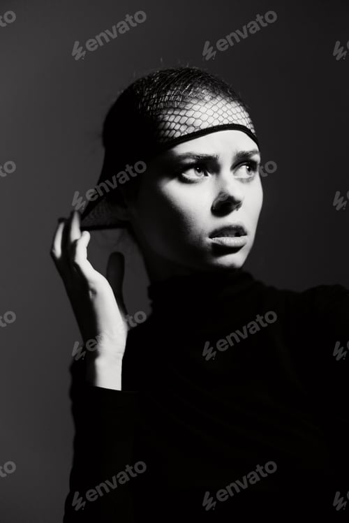 Preview: Pensive young woman in black attire with a fishnet headpiece, looking away thoughtfully against a