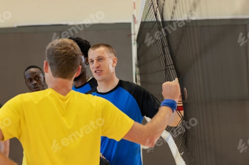 Preview: Diverse male volleyball athletes wearing wristband clasping hands through net at gym