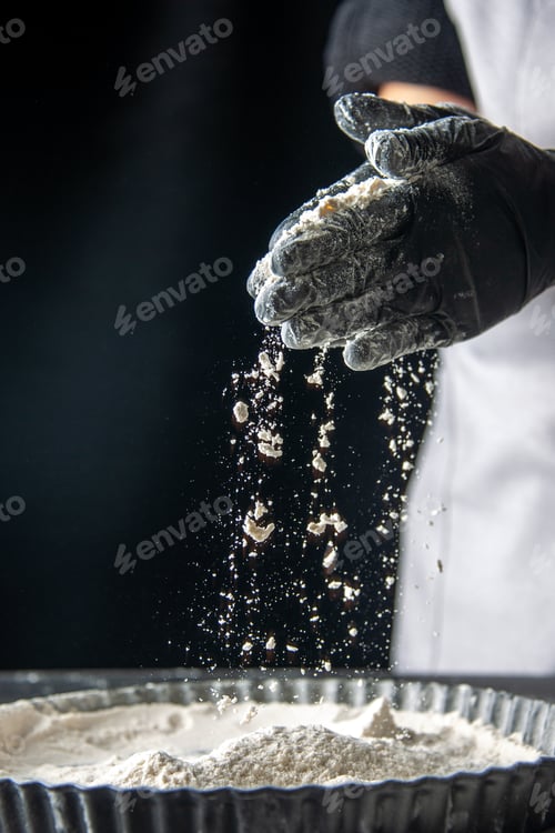 Preview: front view female cook pouring white flour into the pan with her palms on dark background egg cake