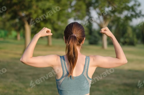 Preview: Woman athlete demonstrates her arm muscles in nature. Rear view of athletic woman showing biceps