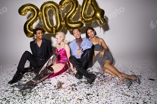 Preview: happy multicultural people sitting near confetti and balloons with 2024 numbers, Happy New Year