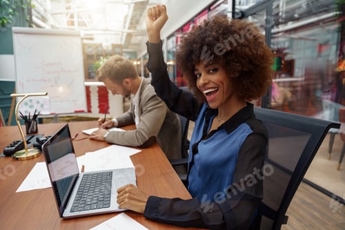 Preview: Happy african businesswoman sitting on his workplace in modern office on colleague background