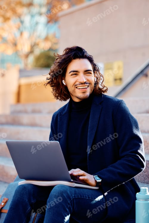 Preview: Happy Latin American entrepreneur using laptop in the city and looking away.