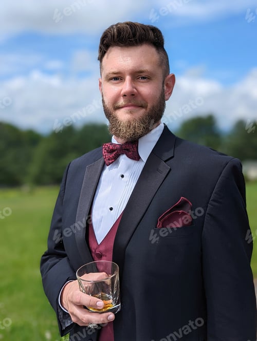 Preview: Man in a tux holding a glass of scotch. Groom in tuxedo outside.