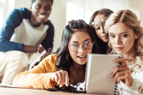 Preview: group of excited mutiethnic students looking at notebook